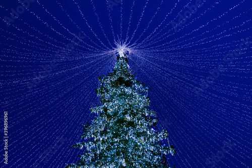 Christmas tree decorated with toys and garlands in the night against the blue sky.