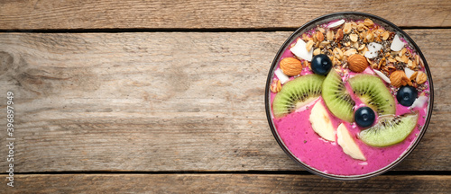 Delicious acai smoothie with granola and fruits in dessert bowl on wooden table, top view. Space for text