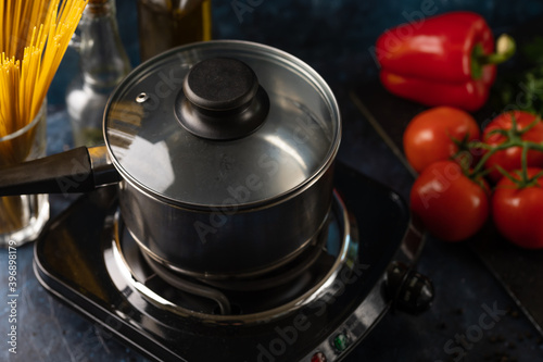 Closed pan with boiling water on marble dark blue table with variety of ingredients background. Backstage of cooking pasta. Concept of cooking process. Close-up view. Cookbook design.