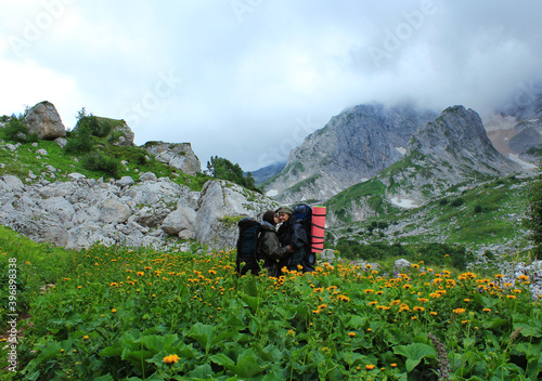 Two female hikers hug in the mountains among flowers. Traveling in the wild of a lesbian couple. A couple of girls kissing on the background of a beautiful landscape.  Active lifestyle photo