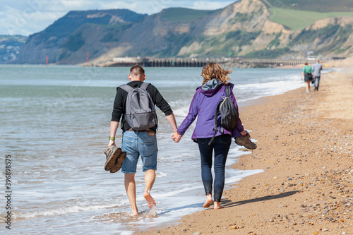 A couple holding hands while barefoot walking alongside beach. Day out at the beach during sunny but windy day. Jurassic Cliffs Coast and golden beach in West Bay. photo