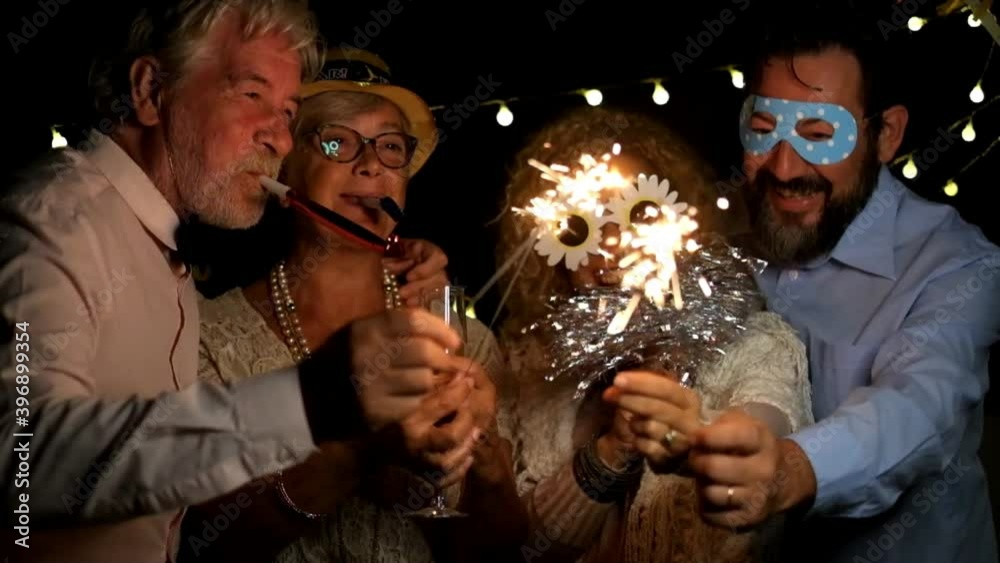 group of four people enjoying new year night celebrating with sparklers in the middle and looking at the camera - adults having fun together