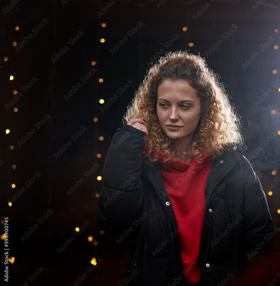 A beautiful curly-haired girl stands on a black background in the New Year's lights A beautiful curly-haired girl stands on a black background in the New Year's lights
