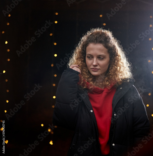 A beautiful curly-haired girl stands on a black background in the New Year's lights