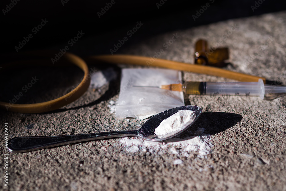 Heroin in syringe and powder heroin on spoon and plastic bag pack with yellow rubber band on dark cement floor. Addictive substance, narcotic, Illegal thing, dangerous drug concept. Heroin in syringe and powder heroin on spoon and plastic bag pack with yellow rubber band on dark cement floor. Addictive substance, narcotic, Illegal thing, dangerous drug concept.