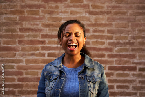 Image of young African American woman screaming excited with closed eyes standing isolated over a brick wall.