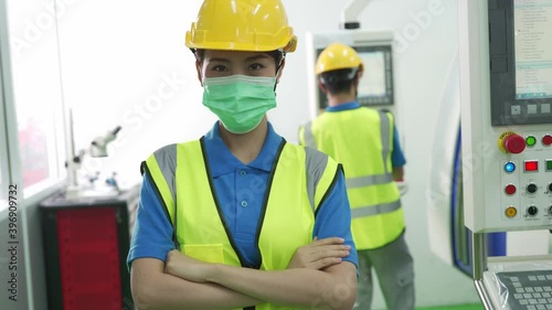 Asian woman production line worker wear protective face mask near control panel machine. Concept of new normal working after Covid 19 pandemic