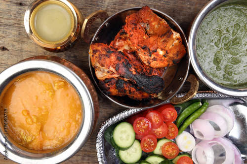 Spicy red Chicken grilled tikka tandoori nan bread green spinach curry yogurt sauce dal tomato cucumber onion salad set in metal stainless steel brass copper pot on rustic vintage wood background