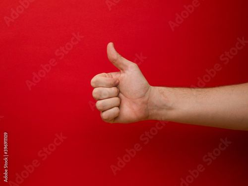 Female hand shows thumb up gesture on a red background