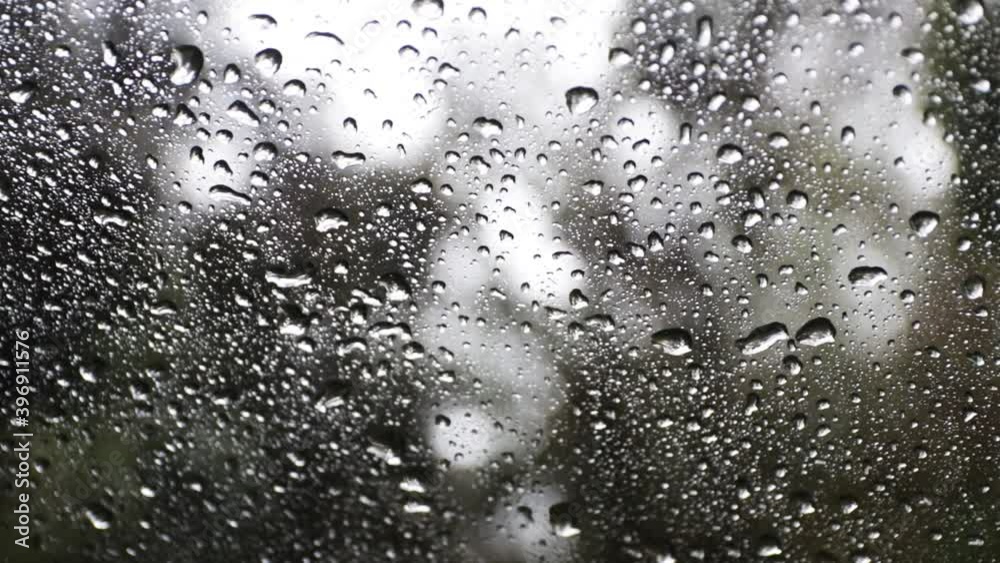 Raining on a cars window with the rain drops flowing down, forest in the background Raining on a cars window with the rain drops flowing down, forest in the background