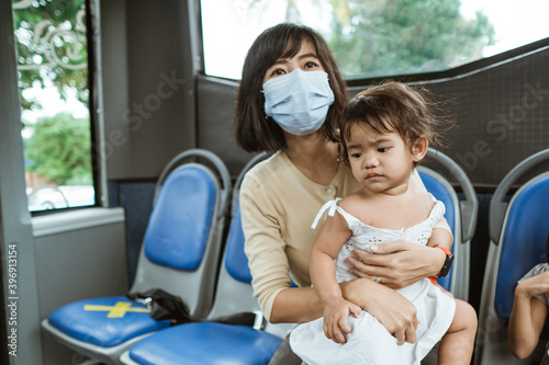 mother and daughter riding public transport during pandemic wearing facemask © Odua Images