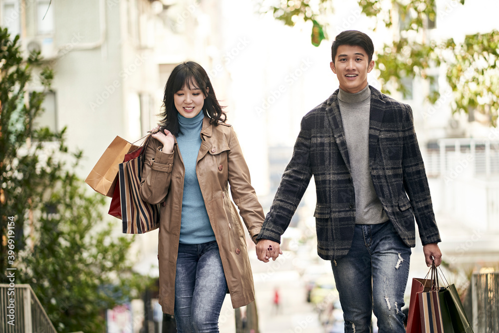happy young asian couple walking on street with shopping bags in hands