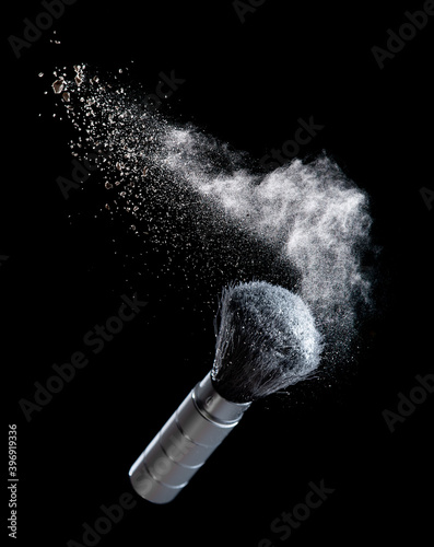 White powder splash and cosmetic brush for makeup on black background
