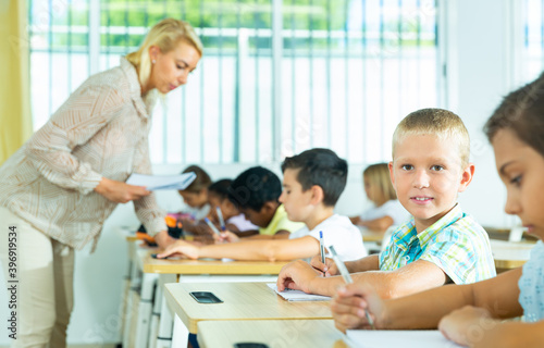 Positive boys sits at a desk next to diligent elementary school students