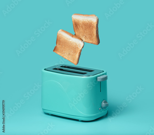 Bread popping up of toaster on mint green background photo
