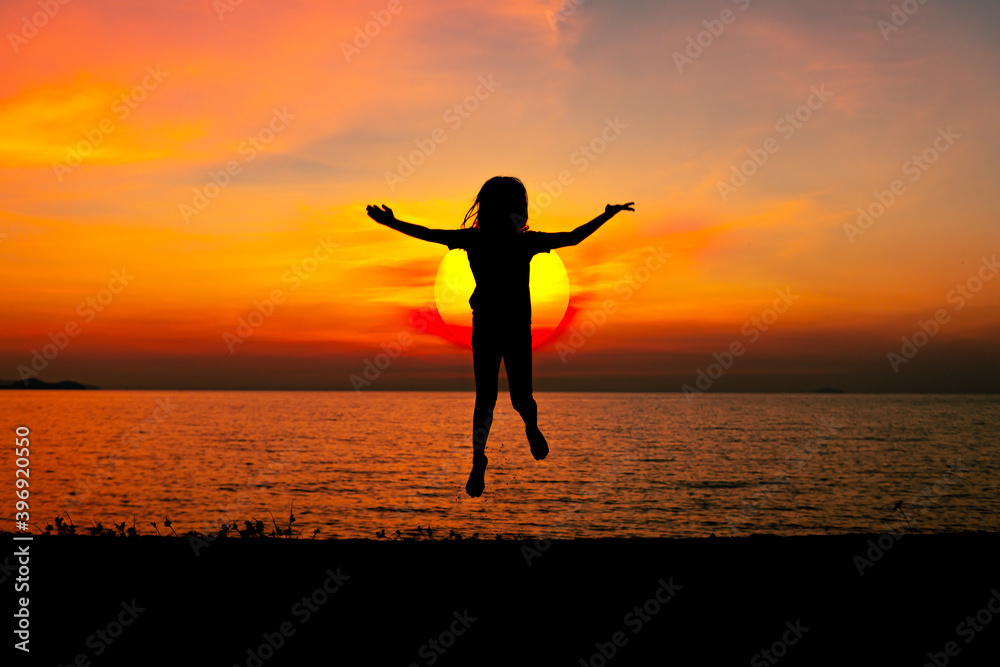 Silhouette happy young girl jumping cheerful on sand near beach with beautiful sunset sky background.