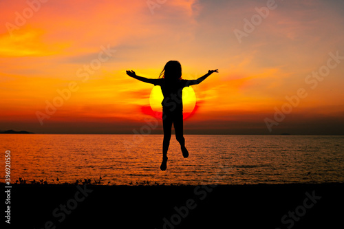 Silhouette happy young girl jumping cheerful on sand near beach with beautiful sunset sky background.