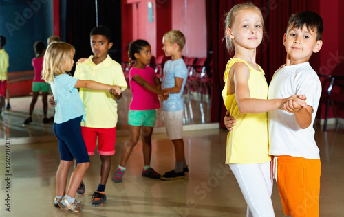 Group of positive smiling childrens trying dancing with partner in classroom