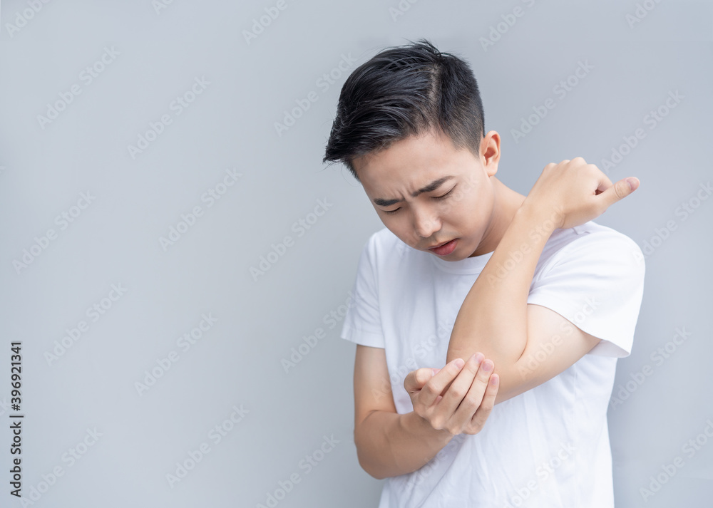 Young man is frowning painfully with hand over his elbow Young man is frowning painfully with hand over his elbow