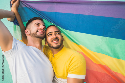 Gay couple embracing and showing their love with rainbow flag.