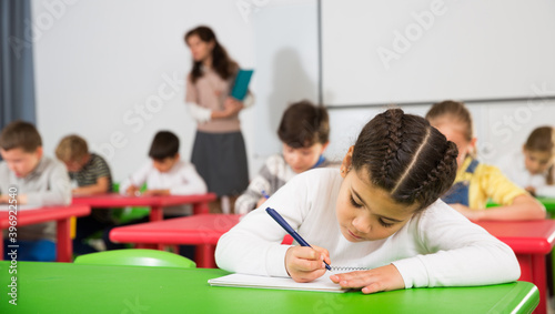 Portrait of diligent schoolgirl writing exercises at lessons in primary school..