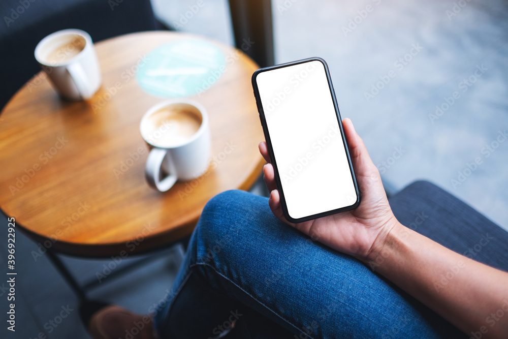 Mockup image of a woman holding mobile phone with blank white desktop screen with coffee cup on the table Mockup image of a woman holding mobile phone with blank white desktop screen with coffee cup on the table