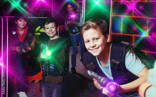 excited sportive young boy aiming laser gun at other players during lasertag game in dark room