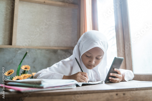 indonesian schoolgirl studying homework during her online lesson at home, social distance during quarantine, online education concept, home schooler