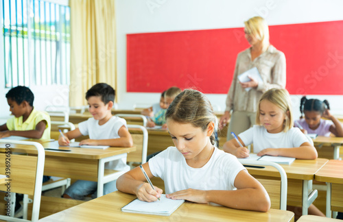 Group of focused pupils sitting at classroom working at class with teacher