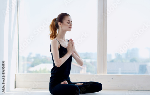 Side view of a woman practicing yoga in the room near the window with her legs crossed