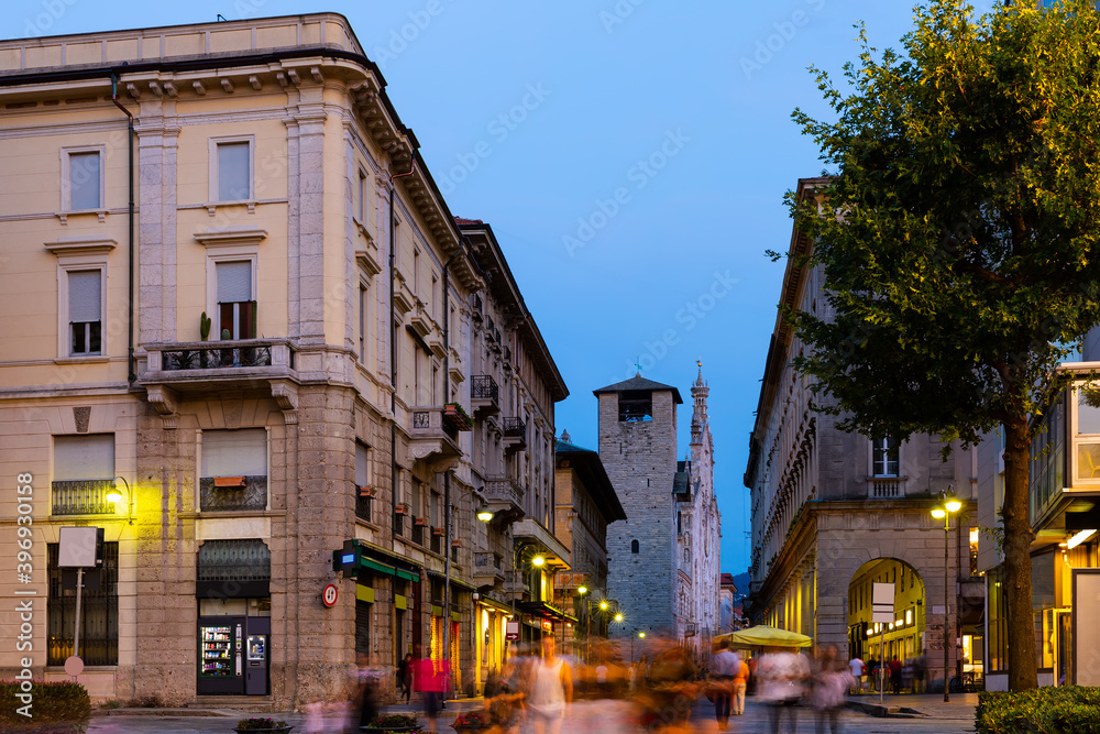 View of busy tourist street of Italian city of Como overlooking bell tower of ancient cathedral at twilight