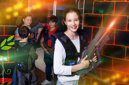 Cheerful happy teen girl standing with laser pistol in dark lasertag room during game with friends