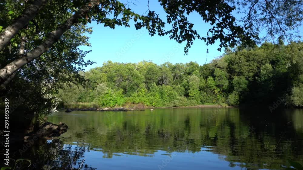 A quiet place where the water is surrounded by shades made by trees. On the other side of the river, we can see a blue sky and trees. A quiet place where the water is surrounded by shades made by trees. On the other side of the river, we can see a blue sky and trees.