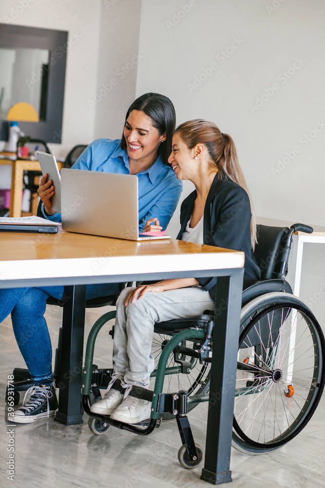 Young Mexican woman in wheelchair at office working with a latin girl in Mexico city Young Mexican woman in wheelchair at office working with a latin girl in Mexico city