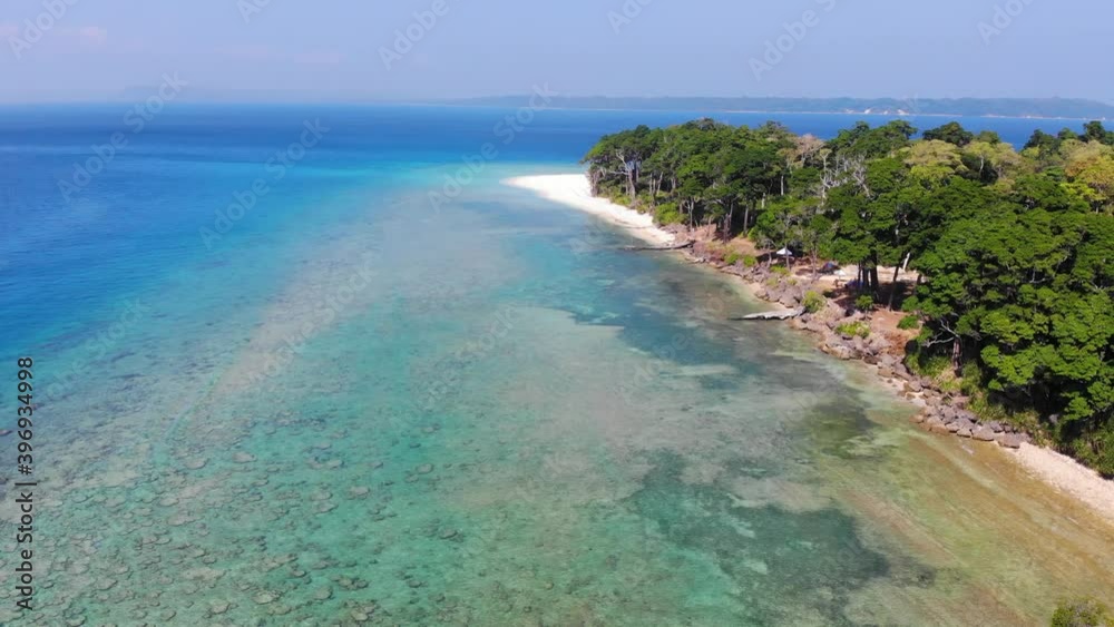 Left to right drone showing remote andaman islands in the distance azure ocean with an ancient forest lining a beach and reefs and rocks to be seen under the shallow water Left to right drone showing remote andaman islands in the distance azure ocean with an ancient forest lining a beach and reefs and rocks to be seen under the shallow water