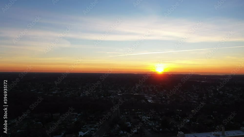 An aerial shot over a suburban neighborhood during a golden sunrise. The camera dolly out from the horizon viewing clouds in the blue sky. The neighborhood is dark below the horizon. An aerial shot over a suburban neighborhood during a golden sunrise. The camera dolly out from the horizon viewing clouds in the blue sky. The neighborhood is dark below the horizon.