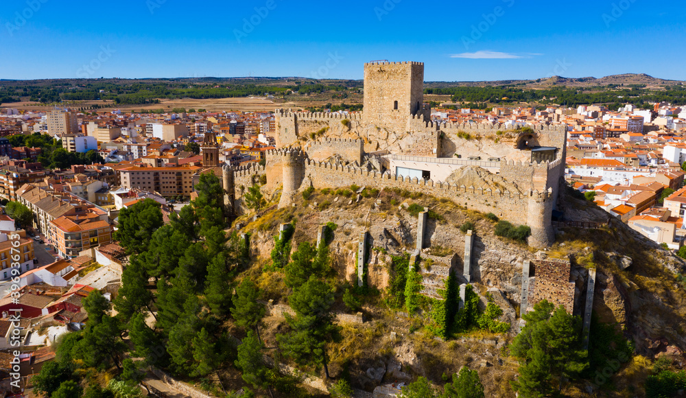 Scenic aerial view of residential areas in small Spanish town of Almansa with dominating medieval walled Castle on hilltop on sunny fall day..