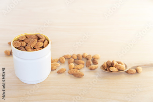 Close up or macro of organic raw peeled almond nuts in cup and spoon with almons laid around cup on wooden background. photo