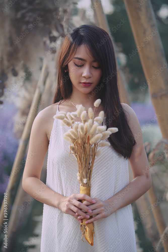 Asian woman in white dress looking down with spikelets in her hands in the garden