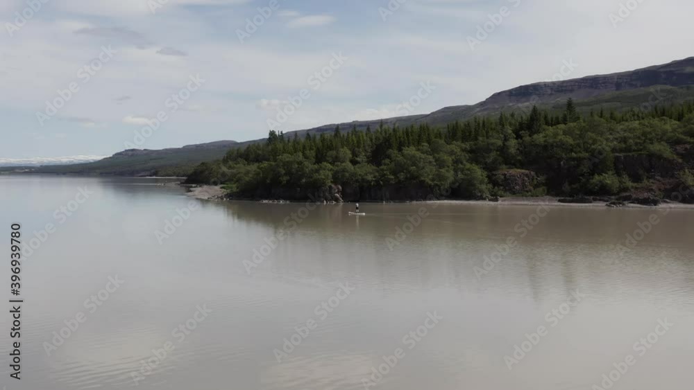 Standup Paddleboarder floating peacefully past forest shore of Lagarfljot river Standup Paddleboarder floating peacefully past forest shore of Lagarfljot river
