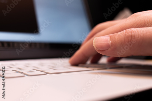 close-up hand of typing blue backlight keyboard on white laptop