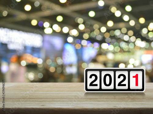 Retro flip clock with 2021 text on wooden table over blur light and shadow of shopping mall, Happy new year 2021 cover concept