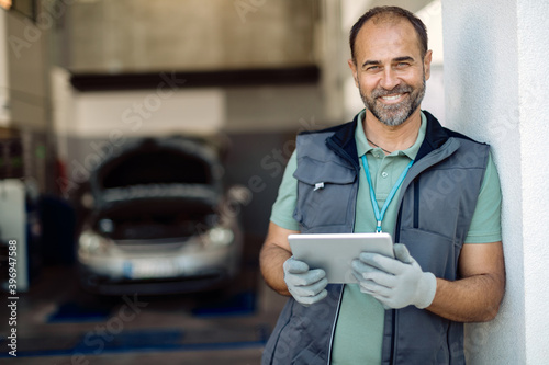 Happy auto mechanic using digital tablet in a workshop and looking at camera.