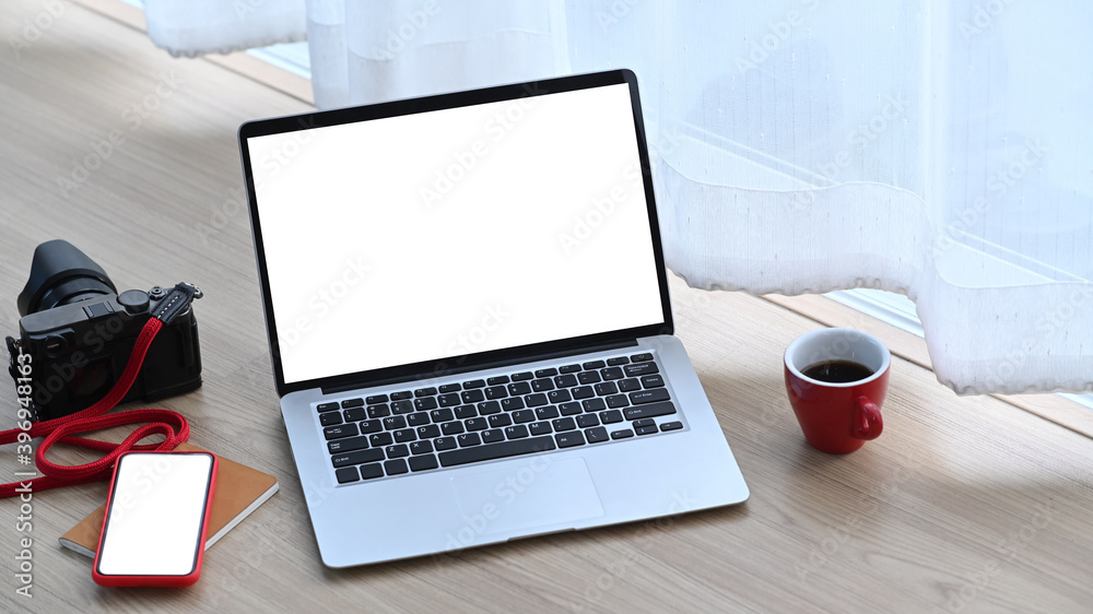 Photographer or designer workstation with white blank screen laptop, camera, mobile phone and coffee cup on the floor. Photographer or designer workstation with white blank screen laptop, camera, mobile phone and coffee cup on the floor.