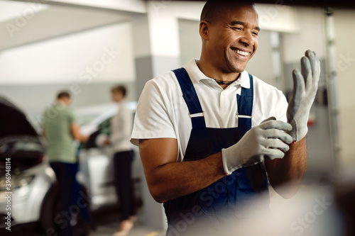 Happy black auto mechanic using gloves while working at repair shop.