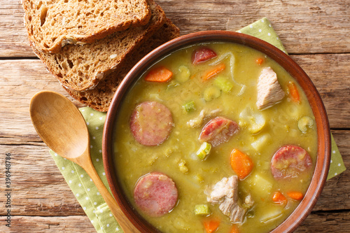 Delicious split green peas soup with vegetables, sausages and pork close-up in a bowl on the table. horizontal top view from above photo