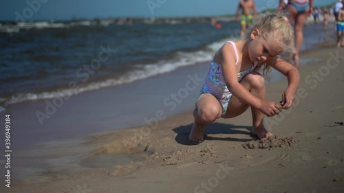 Preschooler girl dig hole in sand. Female child in swimsuit enjoy sea waves