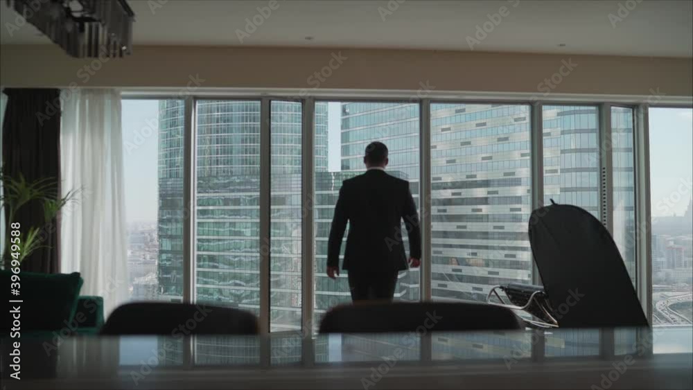 Confident businessman in a large modern office. A modern building. The businessman comes up to the window. Confident businessman in a large modern office. A modern building. The businessman comes up to the window.