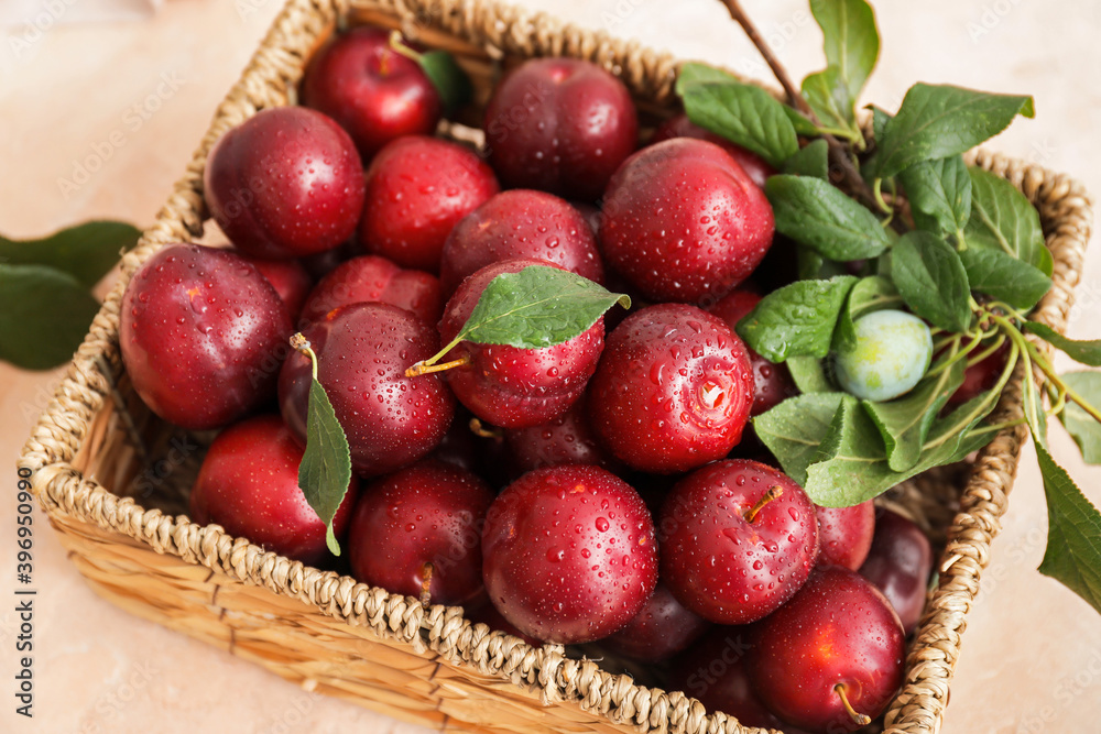 Wicker basket with fresh ripe plums on table