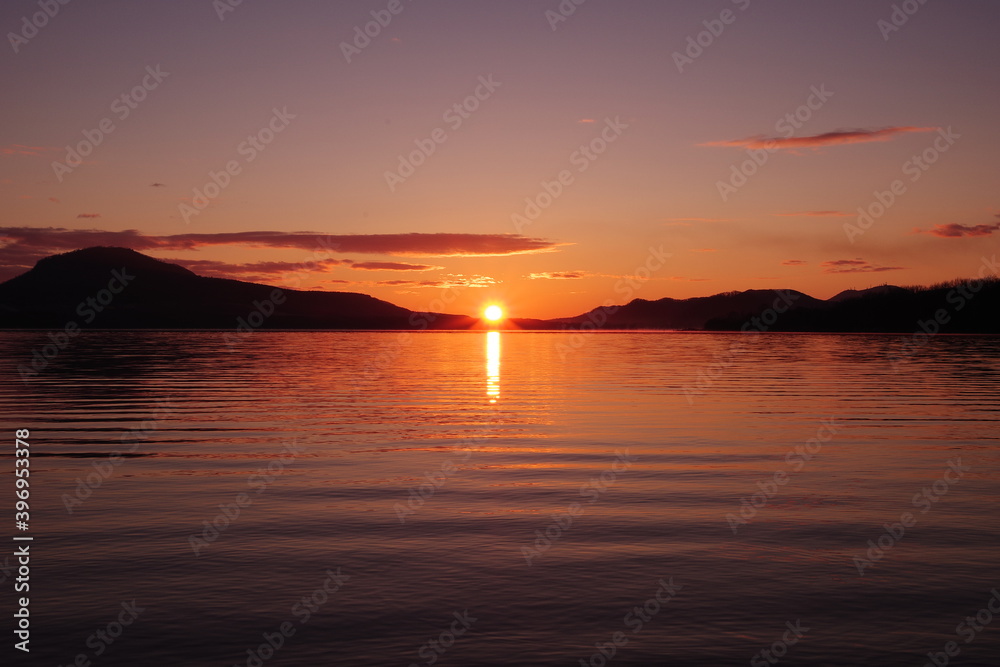 太陽の光に紅く染まる湖の風景。陽光の下のカルデラ湖の明媚な瞬間。